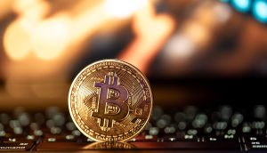Eine physische Bitcoin-Münze steht aufrecht auf einer Laptop-Tastatur, mit verschwommenen, warm getönten Lichtern im Hintergrund, die den digitalen Aufstieg von Bitcoin symbolisieren.