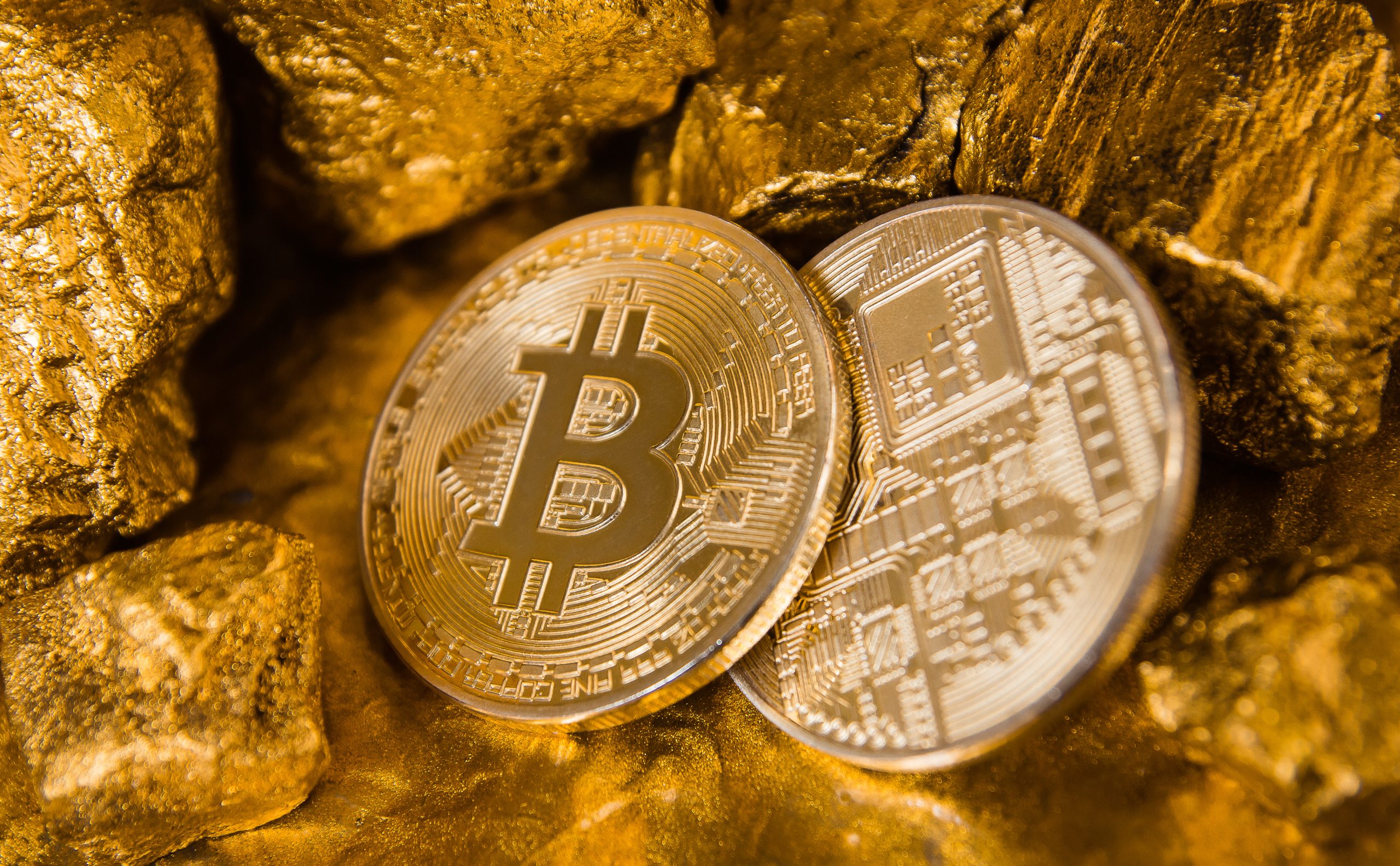 Zwei Bitcoin-Münzen liegen zwischen Goldnuggets und veranschaulichen die Verbindung zwischen Bitcoin und Gold.