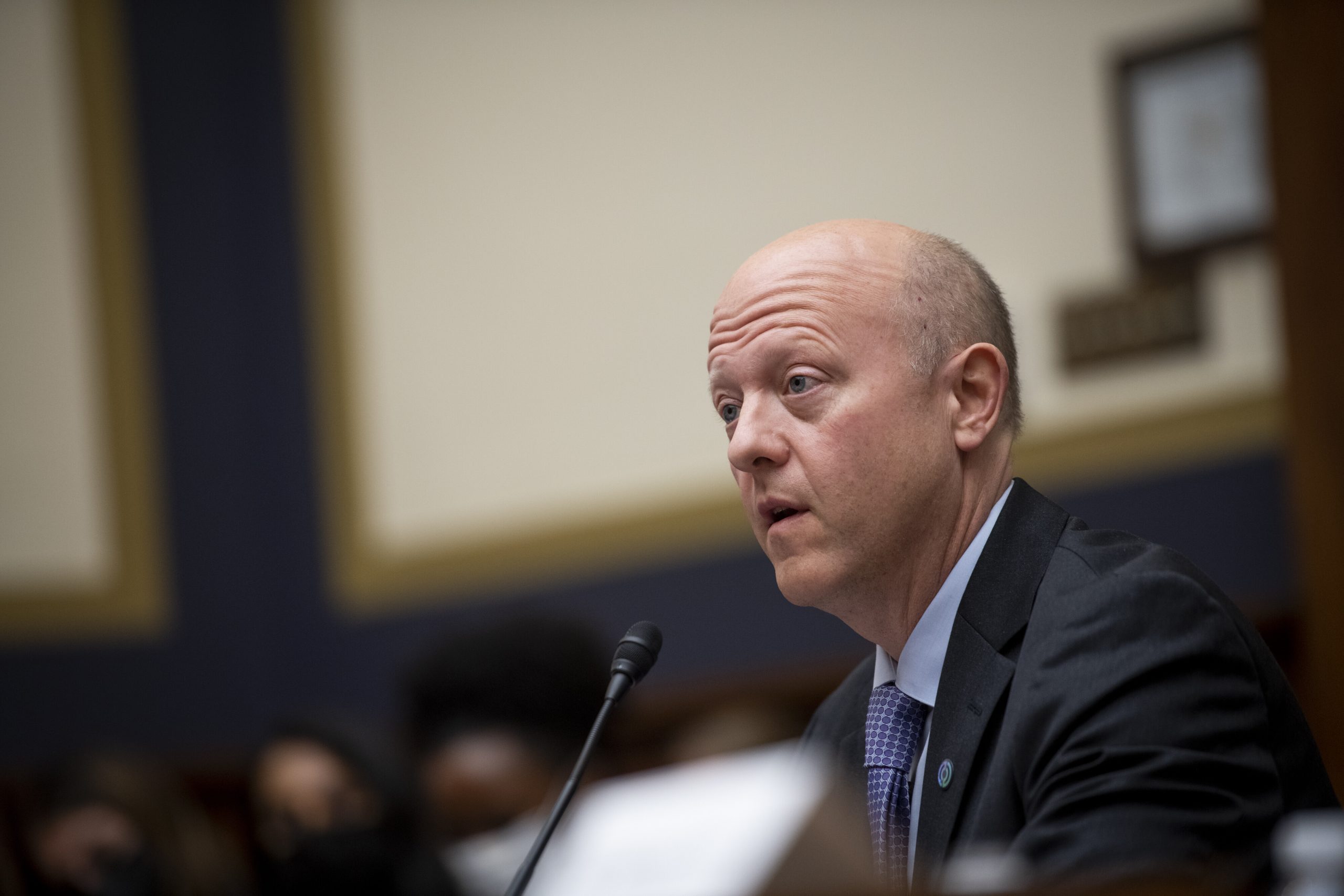 Jeremy Allaire spricht bei einer formellen Besprechung oder Anhörung zu einem möglichen Börsengang in ein Mikrofon, während im Hintergrund unscharfe Personen und Dokumente einen subtilen Kreis bilden.