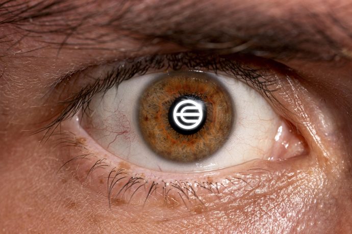 Eine Nahaufnahme eines menschlichen Auges mit einem runden Worldcoin-Logo, in dessen Pupille sich stilisierte Buchstaben spiegeln.