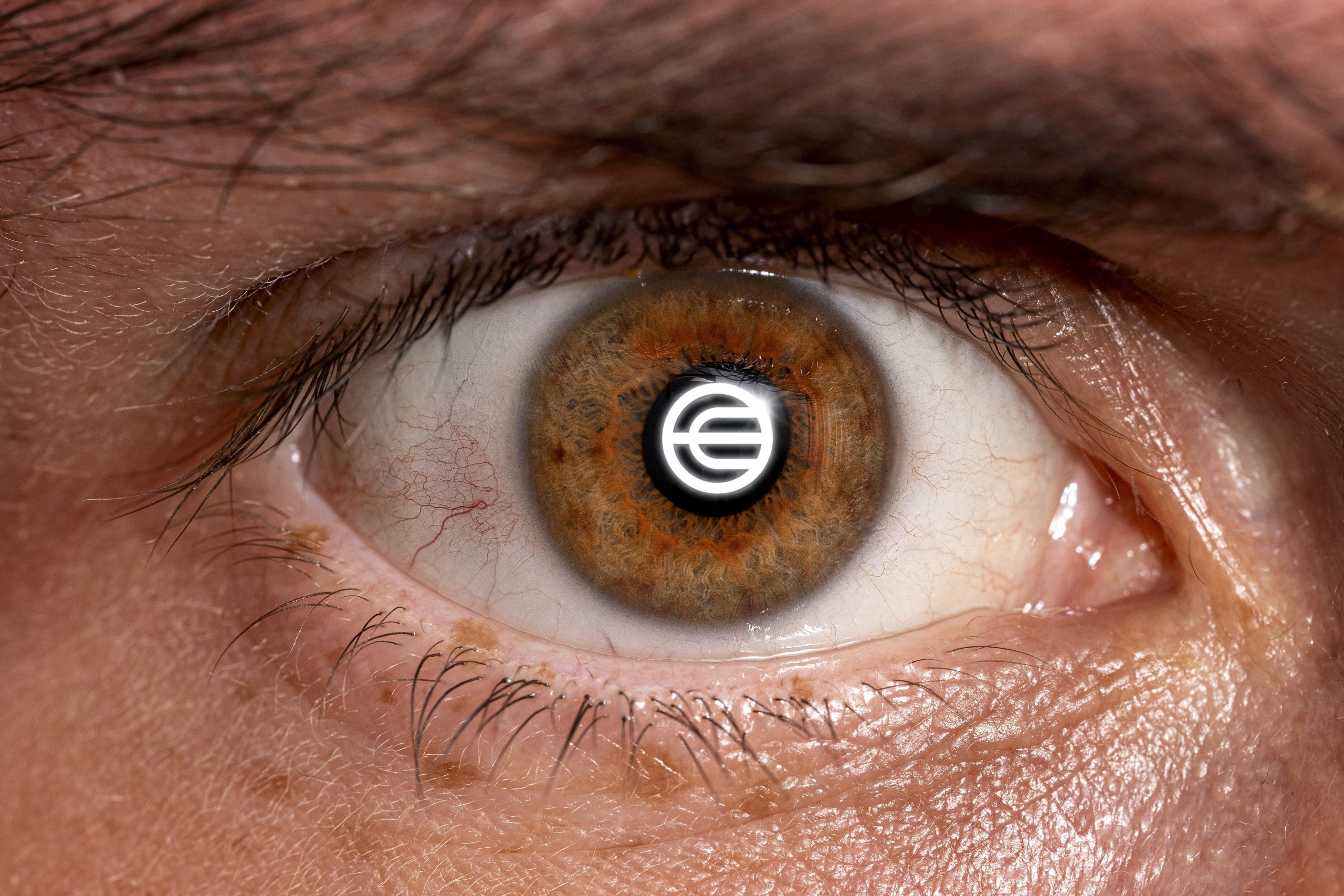Eine Nahaufnahme eines menschlichen Auges mit einem runden Worldcoin-Logo, in dessen Pupille sich stilisierte Buchstaben spiegeln.