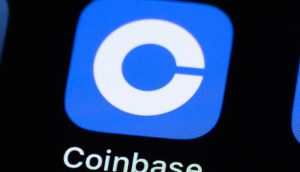 Nahaufnahme des Coinbase-App-Logos, ein weißes C auf blauem quadratischem Hintergrund, angezeigt auf einem Bildschirm mit dem App-Namen Coinbase darunter.