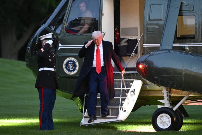 Donald Trump in Anzug und roter Krawatte salutiert beim Verlassen eines Hubschraubers mit dem Präsidentensiegel, während draußen ein uniformierter Marine salutiert – und fängt damit die Formalität ein, bevor Diskussionen über Krypto bei einem Krypto-Dinner von Trump Empörung auslösen.