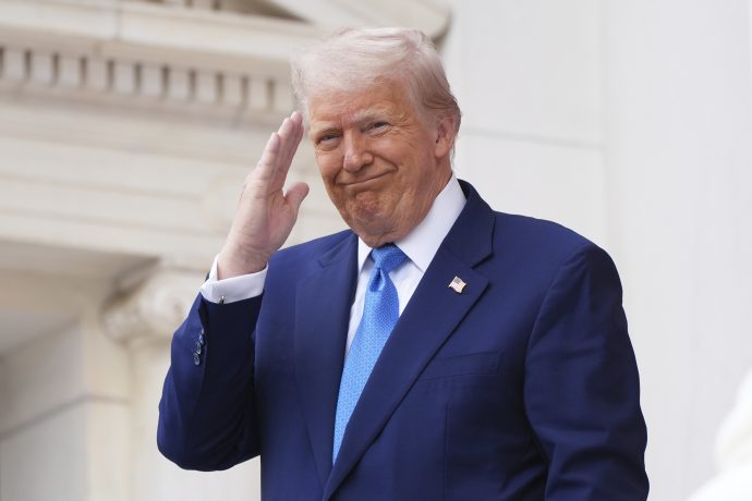 Donald Trump steht im Freien vor einem weißen Gebäude, salutiert mit der rechten Hand und lächelt leicht, als würde er seinen Erfolg feiern, nachdem er sich entschieden hat, in Bitcoin zu investieren.