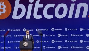 Ein Mann steht mit dem Siegel des Vizepräsidenten an einem Podium und hält vor einem großen Bitcoin-Logo und Sponsorenlogos eine Rede, in der er den wachsenden Einfluss von Bitcoin im politischen und finanziellen Bereich hervorhebt.