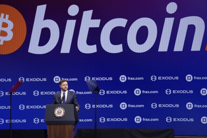Ein Mann steht mit dem Siegel des Vizepräsidenten an einem Podium und hält vor einem großen Bitcoin-Logo und Sponsorenlogos eine Rede, in der er den wachsenden Einfluss von Bitcoin im politischen und finanziellen Bereich hervorhebt.