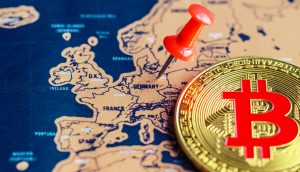 Eine goldene Bitcoin-Münze und eine rote Stecknadel, die Deutschland auf einer Europakarte markiert, verdeutlichen das wachsende Interesse an Bitcoin, insbesondere angesichts seines jüngsten Allzeithochs.