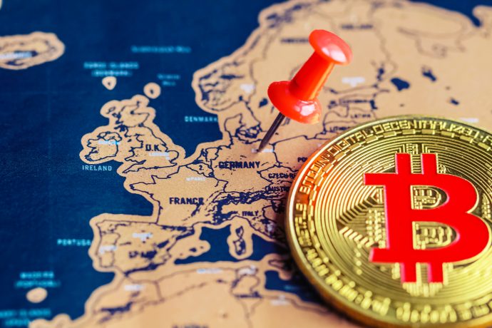 Eine goldene Bitcoin-Münze und eine rote Stecknadel, die Deutschland auf einer Europakarte markiert, verdeutlichen das wachsende Interesse an Bitcoin, insbesondere angesichts seines jüngsten Allzeithochs.