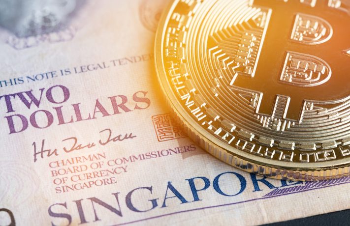 Eine Nahaufnahme eines physischen Bitcoin-Tokens auf einer singapurischen Zwei-Dollar-Banknote, das den Aufstieg der Bitcoin-Strategien unter singapurischen Unternehmen symbolisiert.