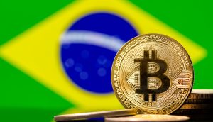 Eine physische Bitcoin-Münze steht vor mehreren Münzen, wobei die brasilianische Flagge im Hintergrund verschwommen ist, was ein wachsendes Interesse an Bitcoin-Strategien in aufstrebenden Fintech-Märkten symbolisiert.
