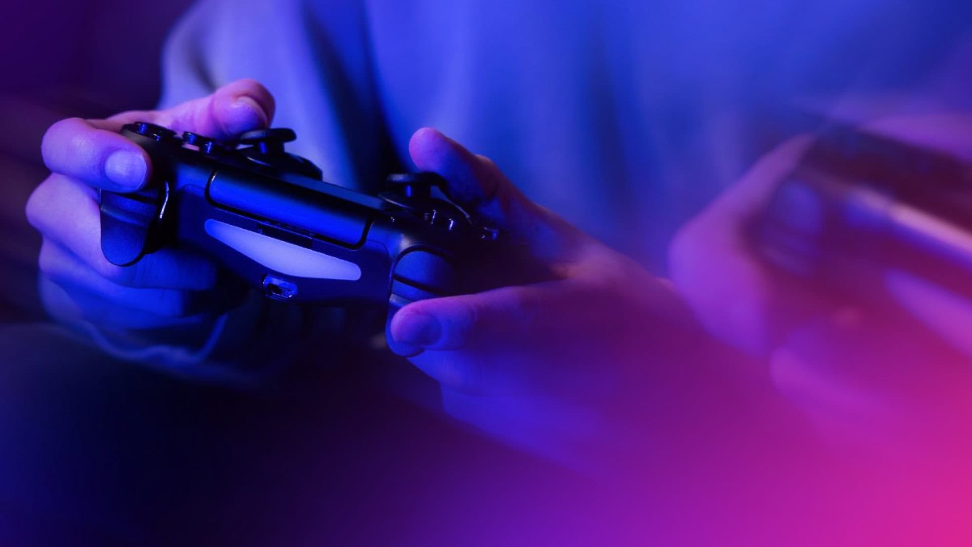 Nahaufnahme von Händen, die einen Videospiel-Controller halten, wobei blaue und violette Polkadot-Beleuchtung im Vordergrund einen weichen, unscharfen Effekt erzeugt.