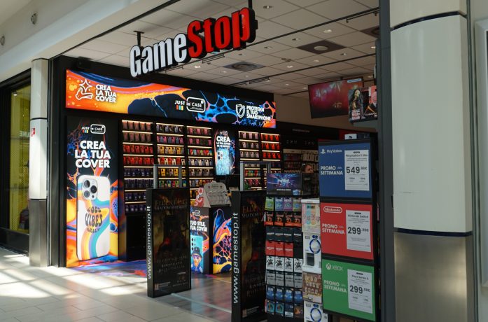 Außenansicht eines GameStop-Geschäfts in einem Einkaufszentrum. Am Eingang werden Videospiele, Werbeplakate und Preisschilder für Konsolen präsentiert. Gamer diskutieren hier über alles von Neuerscheinungen bis hin zu Bitcoin und Gamestops 500-Millionen-US-Dollar-Investition.