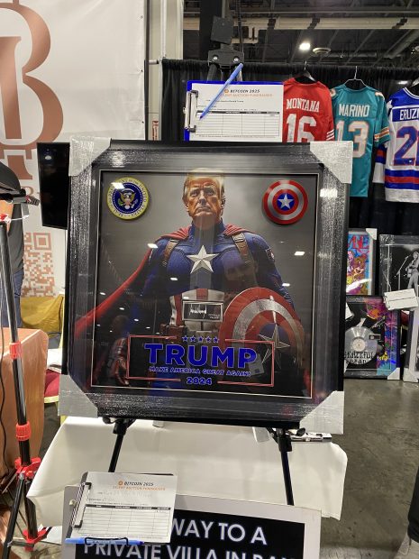 Das gerahmte Kunstwerk zeigt Donald Trump in einem Captain-America-Kostüm mit Präsidentensiegel, Captain-America-Schild, dem Text „Trump 45. Präsident 2024“ und einer Anspielung auf Bitcoin; im Hintergrund sind Sporttrikots zu sehen.
