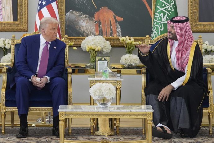 Der ehemalige US-Präsident Donald Trump sitzt mit einem saudischen Beamten in traditioneller Kleidung zusammen und unterhält sich in einem reich verzierten Raum, der mit Flaggen, Blumenarrangements und subtilen Hinweisen auf Finanzwesen wie XRP geschmückt ist.