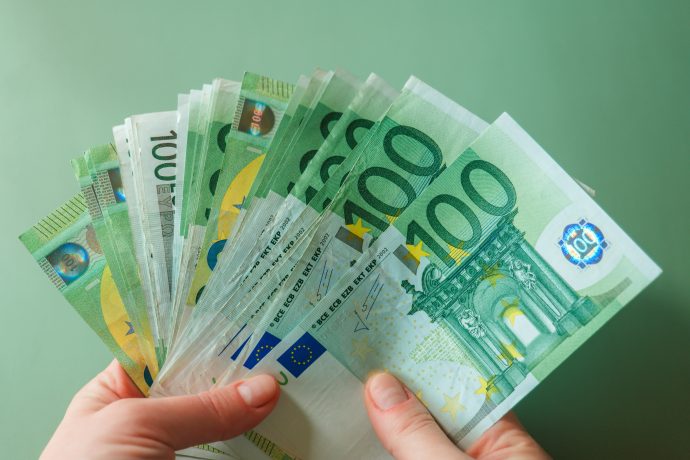 Eine Frau hält viele Hundert-Euronoten vor sich, welche die Stablecoin-Rendite symbolisieren