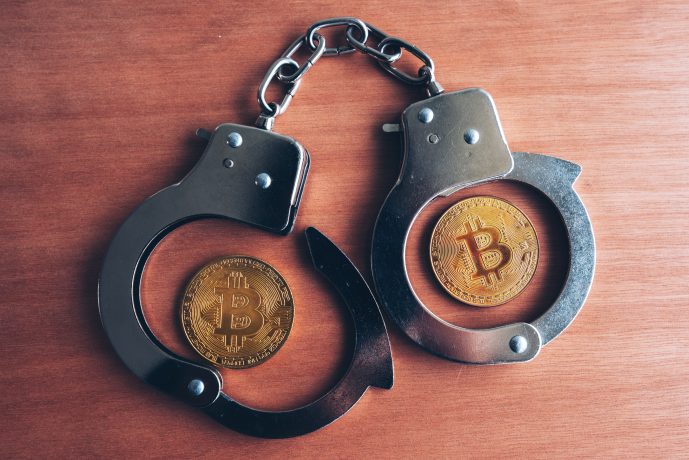 Zwei Bitcoin-Münzen in offenen Handschellen auf einer Holzoberfläche, die Themen wie die Sicherheit von Krypto-Millionären und die potenziellen Risiken von Entführungen in der Welt der Kryptowährungen und der Regulierung aufgreifen.