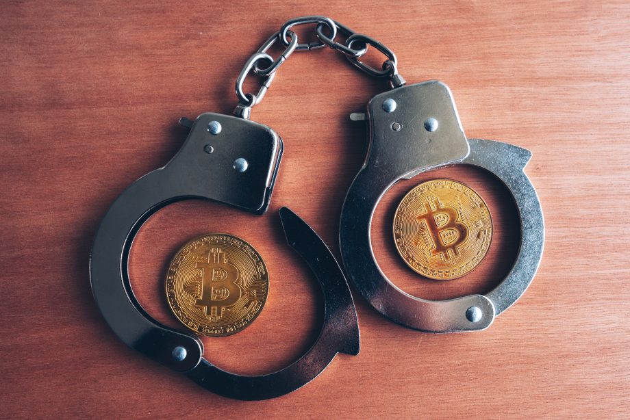 Zwei Bitcoin-Münzen in offenen Handschellen auf einer Holzoberfläche, die Themen wie die Sicherheit von Krypto-Millionären und die potenziellen Risiken von Entführungen in der Welt der Kryptowährungen und der Regulierung aufgreifen.