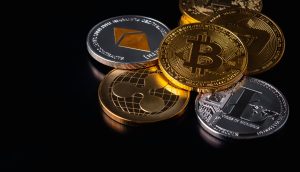 Eine Gruppe physischer Münzen, die verschiedene Kryptowährungen darstellen, darunter Bitcoin, Ethereum, Ripple und Litecoin, angeordnet auf einer schwarzen Oberfläche.