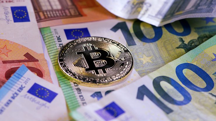 Eine Bitcoin-Münze liegt auf verschiedenen Euro-Scheinen.