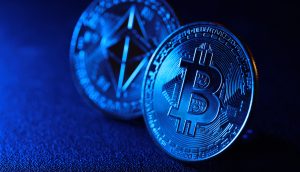 Nahaufnahme physischer Darstellungen von Bitcoin- und Ethereum-Münzen, die aufrecht auf einer dunklen, strukturierten Oberfläche platziert und mit blauem Licht beleuchtet sind – wie ein automatisch gespeicherter Entwurf der digitalen Kryptowelt.