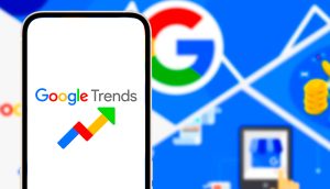 Auf einem Smartphone wird das Google Trends-Logo angezeigt, das das Interesse an Krypto in verschiedenen Ländern hervorhebt, mit einem unscharfen Hintergrund, auf dem ein großes Google-Logo und digitale Symbole zu sehen sind.