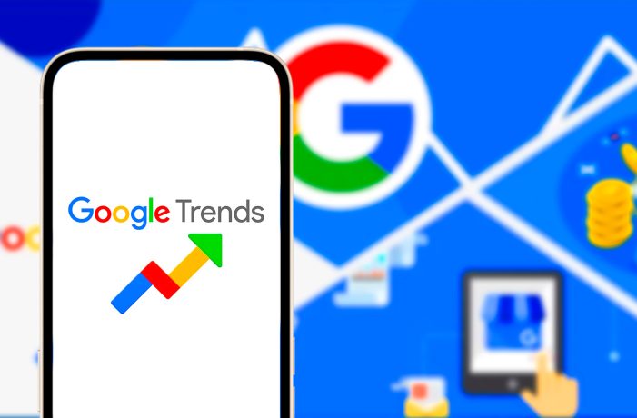 Auf einem Smartphone wird das Google Trends-Logo angezeigt, das das Interesse an Krypto in verschiedenen Ländern hervorhebt, mit einem unscharfen Hintergrund, auf dem ein großes Google-Logo und digitale Symbole zu sehen sind.
