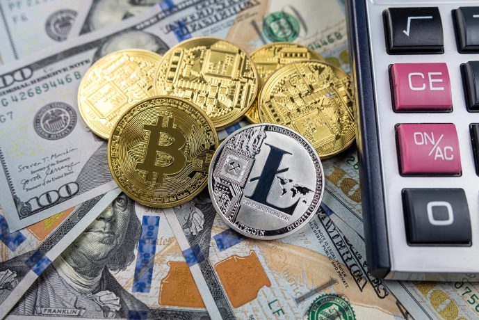 Gold- und Silbermünzen in Form von Kryptowährungen, darunter Bitcoin und Litecoin, werden neben einem Taschenrechner auf US-Dollarscheinen platziert, um das Konzept der Krypto-Steuer hervorzuheben.