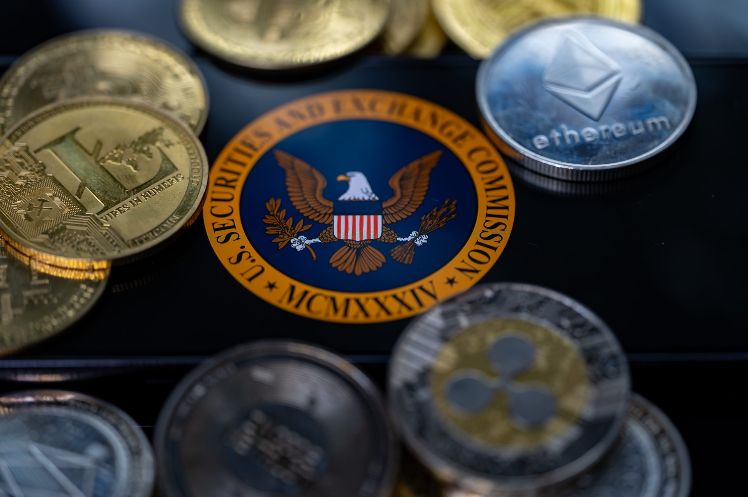 Eine Nahaufnahme verschiedener Kryptowährungen, darunter Bitcoin, Ethereum und Ripple, die das Siegel der US-Börsenaufsichtsbehörde SEC auf einer reflektierenden Oberfläche umgeben.