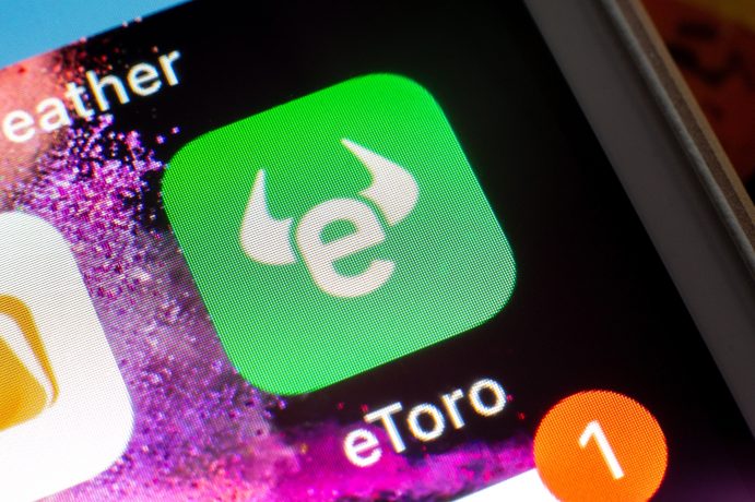 Nahaufnahme eines Smartphone-Bildschirms mit dem grünen Symbol der eToro-App, einem weißen stilisierten Bullenlogo und dem Namen eToro darunter.