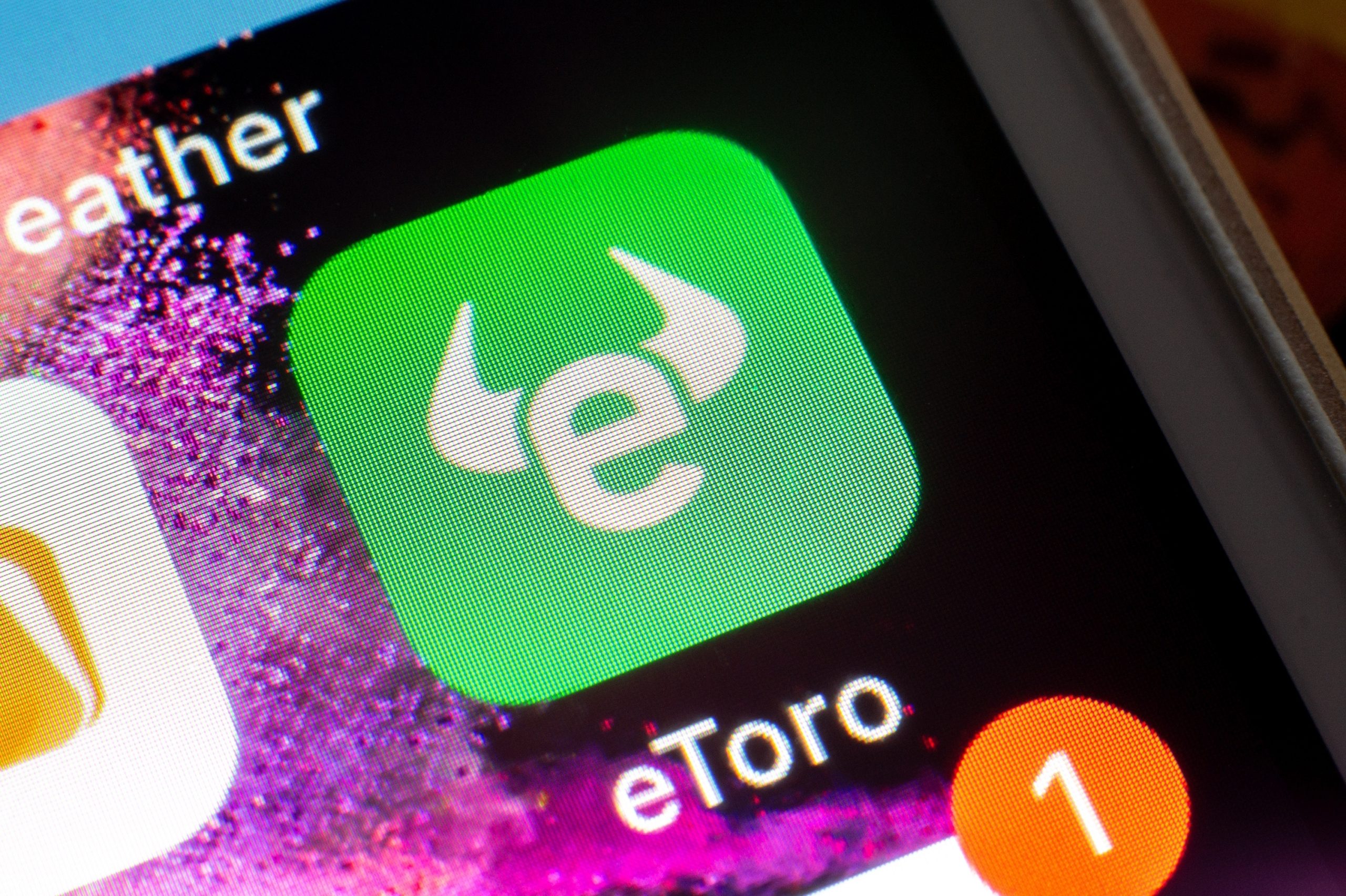 Nahaufnahme eines Smartphone-Bildschirms mit dem grünen Symbol der eToro-App, einem weißen stilisierten Bullenlogo und dem Namen eToro darunter.