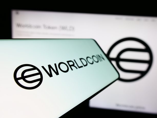 Nahaufnahme eines Smartphones, auf dem das Worldcoin-Logo und der Worldcoin-Text angezeigt werden, mit einer unscharfen größeren Version desselben Logos im Hintergrund.