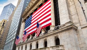 Auf der Fassade eines großen Steingebäudes sind mehrere amerikanische Flaggen zu sehen, darunter zwei große, im Hintergrund sind hohe Wolkenkratzer und Schlagzeilen zu Stablecoins zu sehen.