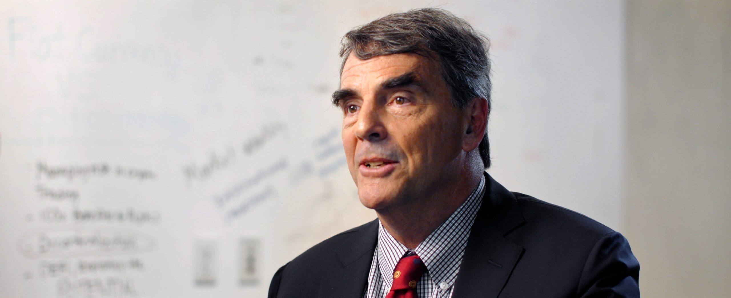 Tim Draper spricht vor einem Whiteboard mit undeutlicher Schrift und diskutiert Tim Drapers neueste Bitcoin-Kursprognose.