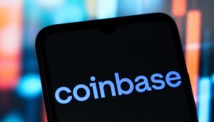 Ein Smartphone-Bildschirm zeigt das Coinbase-Logo in weißer Schrift auf schwarzem Hintergrund, mit bunten, verschwommenen Lichtern im Hintergrund, die an einen automatisch gespeicherten Entwurf erinnern.