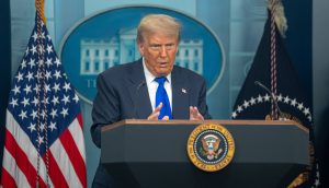Donald Trump spricht an einem Podium mit dem Siegel des US-Präsidenten, flankiert von amerikanischen Flaggen und dem Emblem des Weißen Hauses, über Bitcoin und seine Auswirkungen auf die Bitcoin-Branche, während US-Präsident Trump eine Rede an die Nation hält.