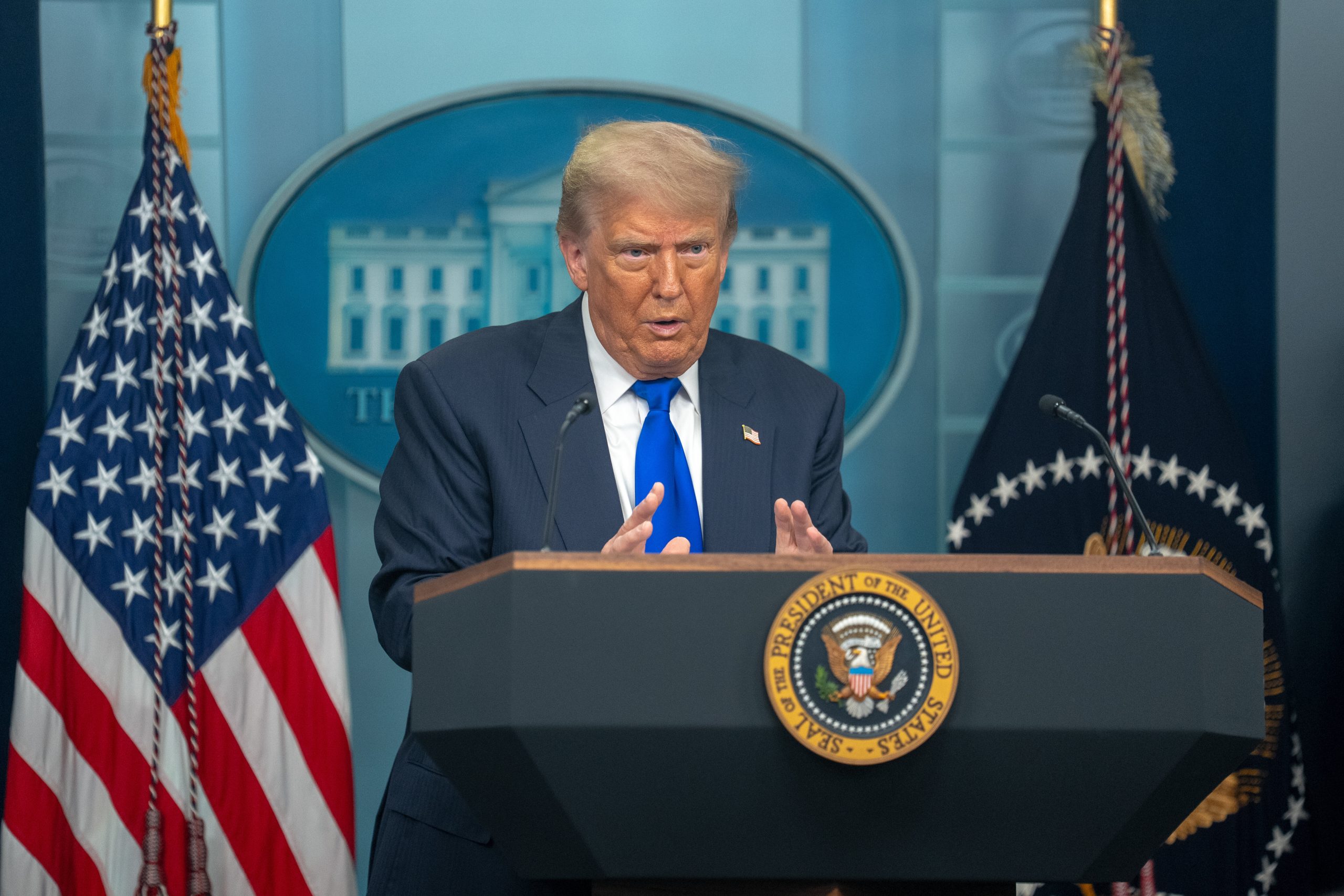 Donald Trump spricht an einem Podium mit dem Siegel des US-Präsidenten, flankiert von amerikanischen Flaggen und dem Emblem des Weißen Hauses, über Bitcoin und seine Auswirkungen auf die Bitcoin-Branche, während US-Präsident Trump eine Rede an die Nation hält.