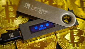 Eine Ledger-Hardware-Wallet wird auf mehreren goldfarbenen Bitcoin-Münzen präsentiert und betont die sichere Aufbewahrung von Kryptowährungen.