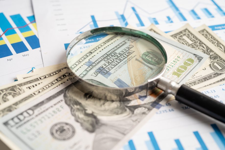 Lupe über US-Dollar-Noten auf Finanztabellen und -grafiken, die die Finanzanalyse und die Untersuchung von Geld- oder Krypto-Daten darstellen.