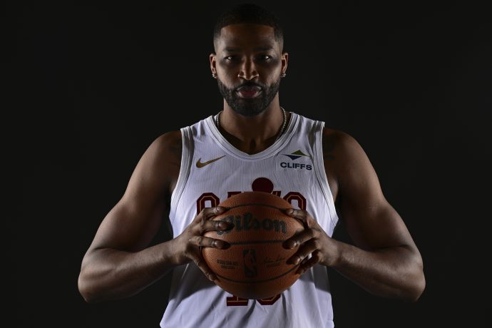 NBA-Star Tristan Thomas, in einem weißen Trikot, hält mit beiden Händen einen Basketball vor einem dunklen Hintergrund, bereit für das Interview.