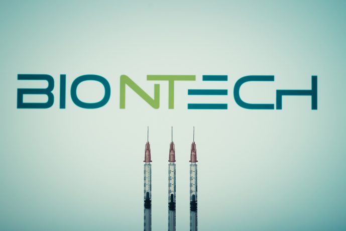 Drei Spritzen sind vor einem unscharfen BioNTech-Logo aufgereiht und heben die medizinischen Innovationen von BioNTech auf einem hellen Hintergrund hervor.