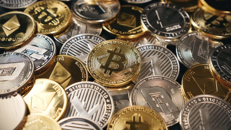 Eine Nahaufnahme verschiedener physischer Münzen, die Kryptowährungen repräsentieren, darunter Bitcoin, Ethereum und Litecoin, in Gold- und Silberfarben. Die herausragende Bitcoin-Münze sticht aus der detaillierten Sammlung hervor.