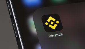 Nahaufnahme eines Smartphone-Bildschirms mit dem Binance-App-Symbol und dem charakteristischen gelben geometrischen Binance-Logo auf schwarzem Hintergrund.