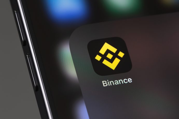 Nahaufnahme eines Smartphone-Bildschirms mit dem Binance-App-Symbol und dem charakteristischen gelben geometrischen Binance-Logo auf schwarzem Hintergrund.