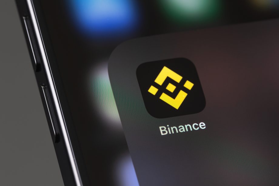 Nahaufnahme eines Smartphone-Bildschirms mit dem Binance-App-Symbol und dem charakteristischen gelben geometrischen Binance-Logo auf schwarzem Hintergrund.