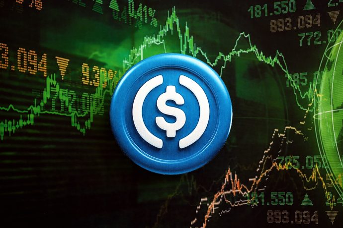 Ein USDC-Münzsymbol, das die beliebte Stablecoin darstellt, wird vor einem digitalen Bildschirm angezeigt, auf dem schwankende Finanz- und Kryptowährungsmarktdiagramme zu sehen sind.