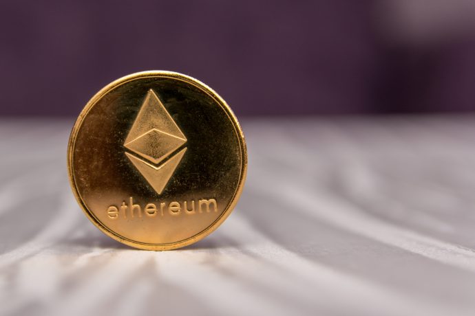 Eine goldfarbene Ethereum-Münze mit dem Ethereum-Logo und dem Wort "Ethereum" ruht auf einer hellen, strukturierten Oberfläche.