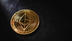 Eine Goldmünze mit dem Ethereum-Logo liegt auf einer dunklen, strukturierten Oberfläche und symbolisiert den Wert und die Innovation von Ethereum.