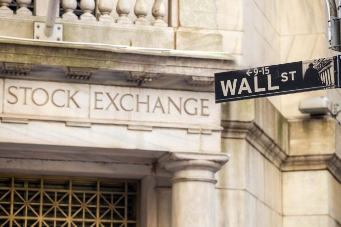 Vor der Steinfassade der New Yorker Börse ist ein Straßenschild der Wall Street angebracht, das die Überschneidung von traditionellem Finanzwesen und modernen Vermögenswerten wie Bitcoin hervorhebt.
