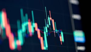 Eine Nahaufnahme eines digitalen Finanzcharts mit Candlestick-Mustern in Rot und Grün auf dunklem Hintergrund, der die XRP-Trends inmitten volatiler US-Zahlen auf dem Krypto-Markt verfolgt.