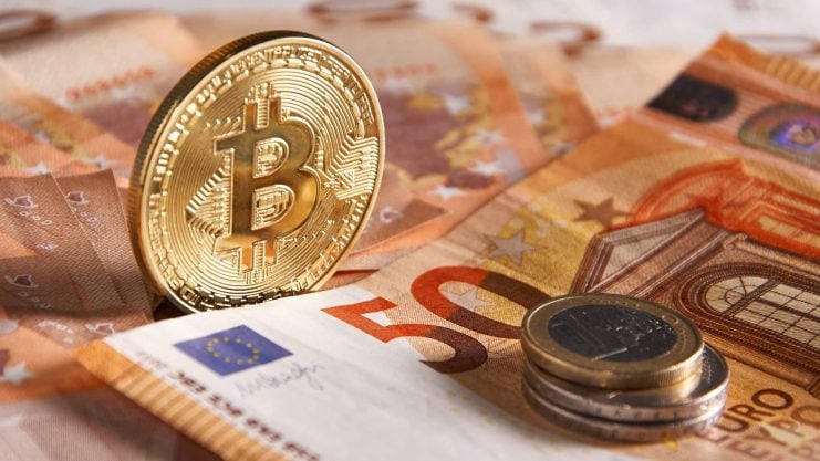 Eine physische Bitcoin-Münze steht aufrecht auf mehreren 50-Euro-Banknoten, daneben liegt ein kleiner Stapel Euro-Münzen, der die Überschneidung von Krypto-Vermögenswerten und traditioneller Währung symbolisiert.